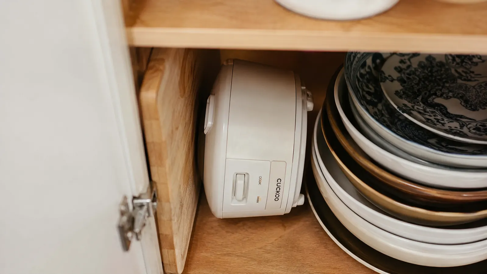 Small ceramic rice cooker pot standing upright in a narrow cabinet gap next to a cutting board