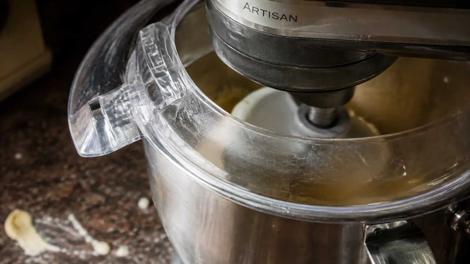 Close view of the Kitchen in the Box mixer's plastic splash guard with batter visible on the counter just past its edge