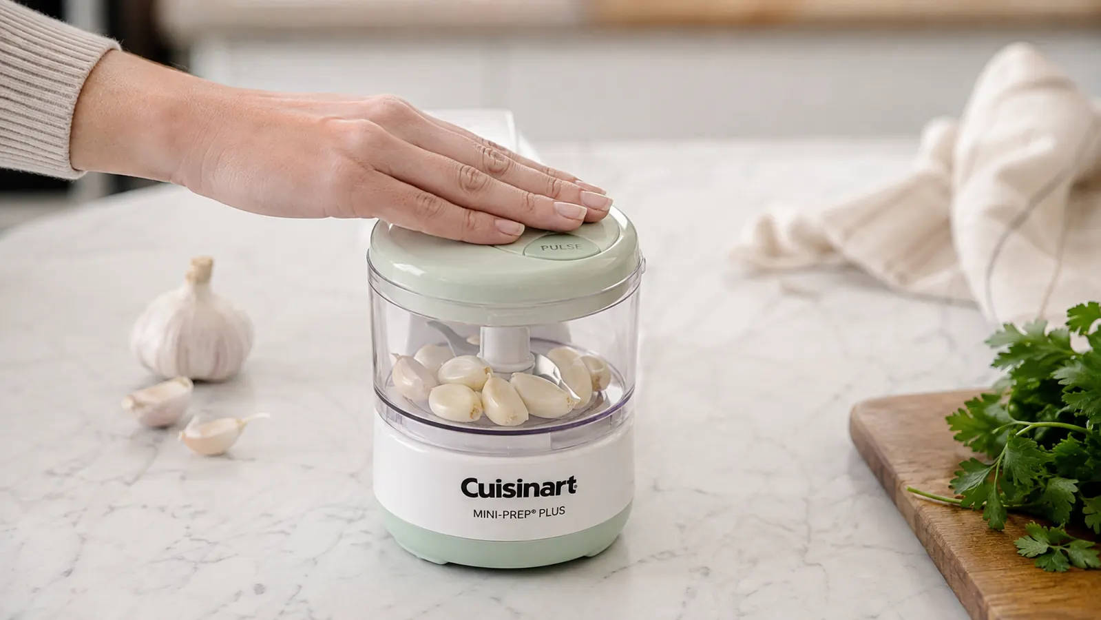 Hand pulsing the Cuisinart Mini-Prep Plus with garlic cloves visible inside the clear work bowl