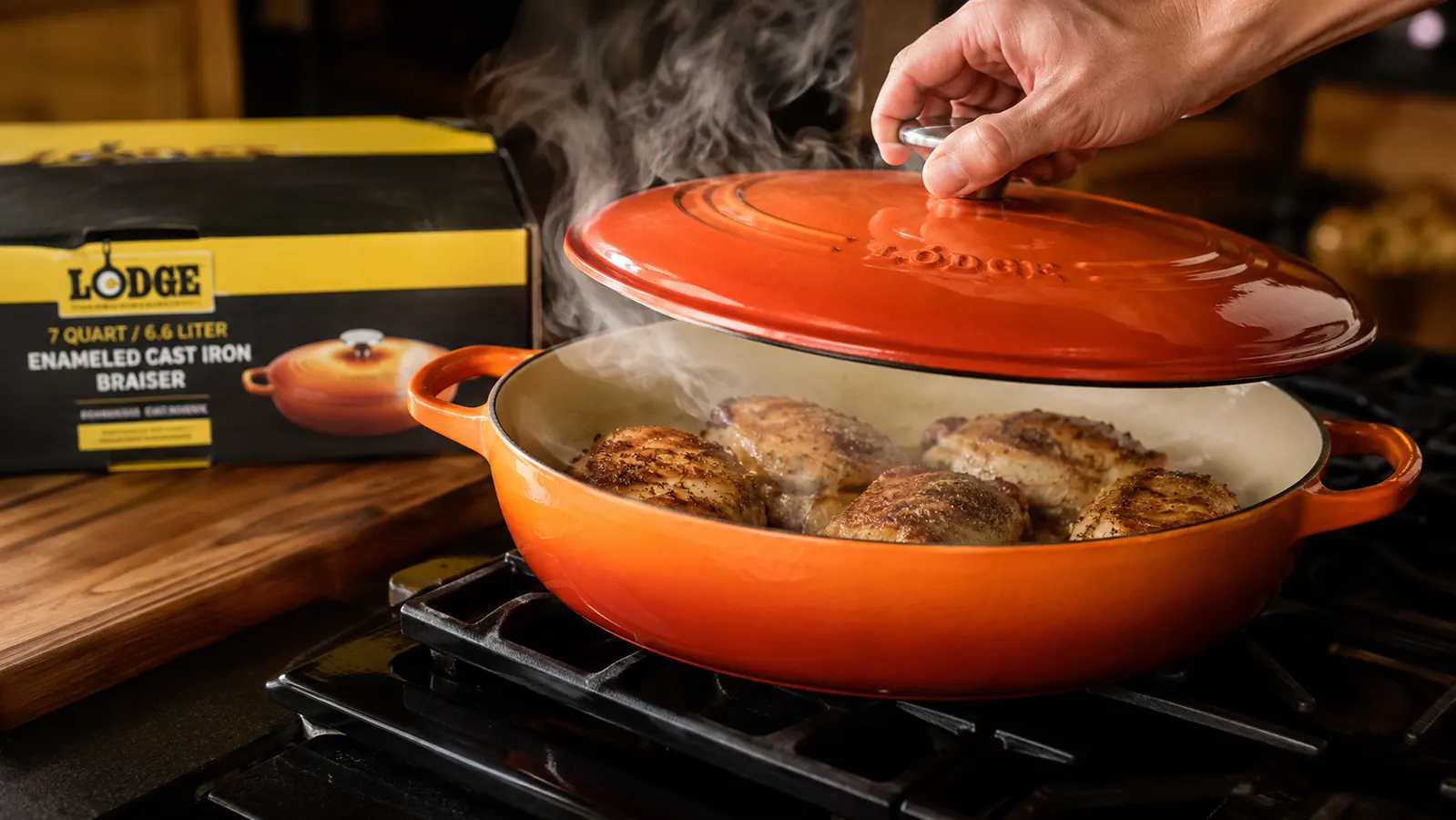Hand lifting the lid off a cornflower blue enameled braiser after searing meat on the stovetop